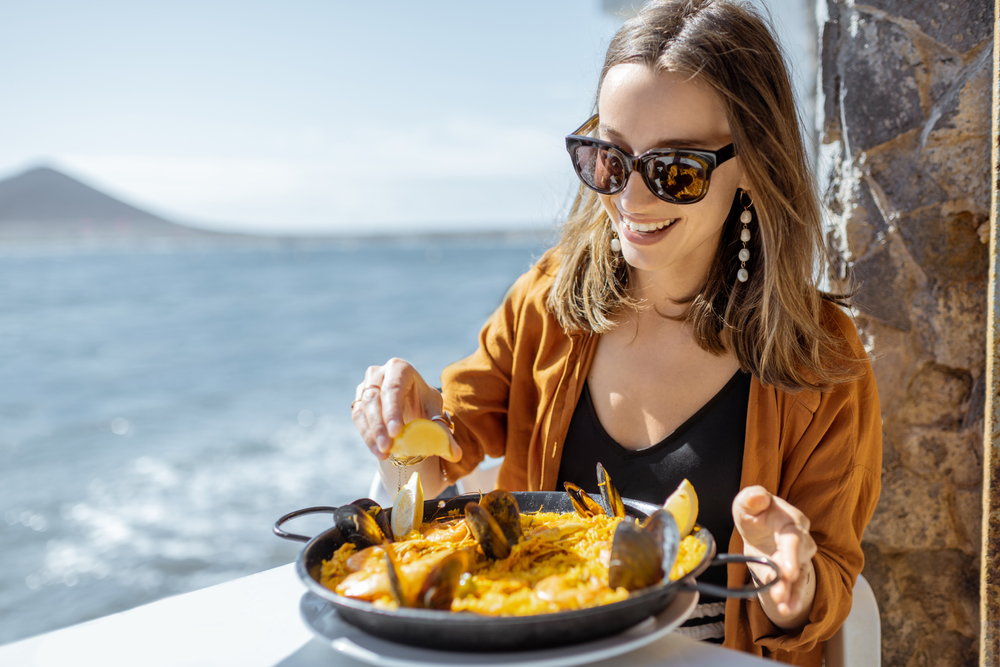 Woman eating paella, while sitting at the restaurant terrace near the ocean.