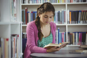 Attentive school girl reading book in library at school